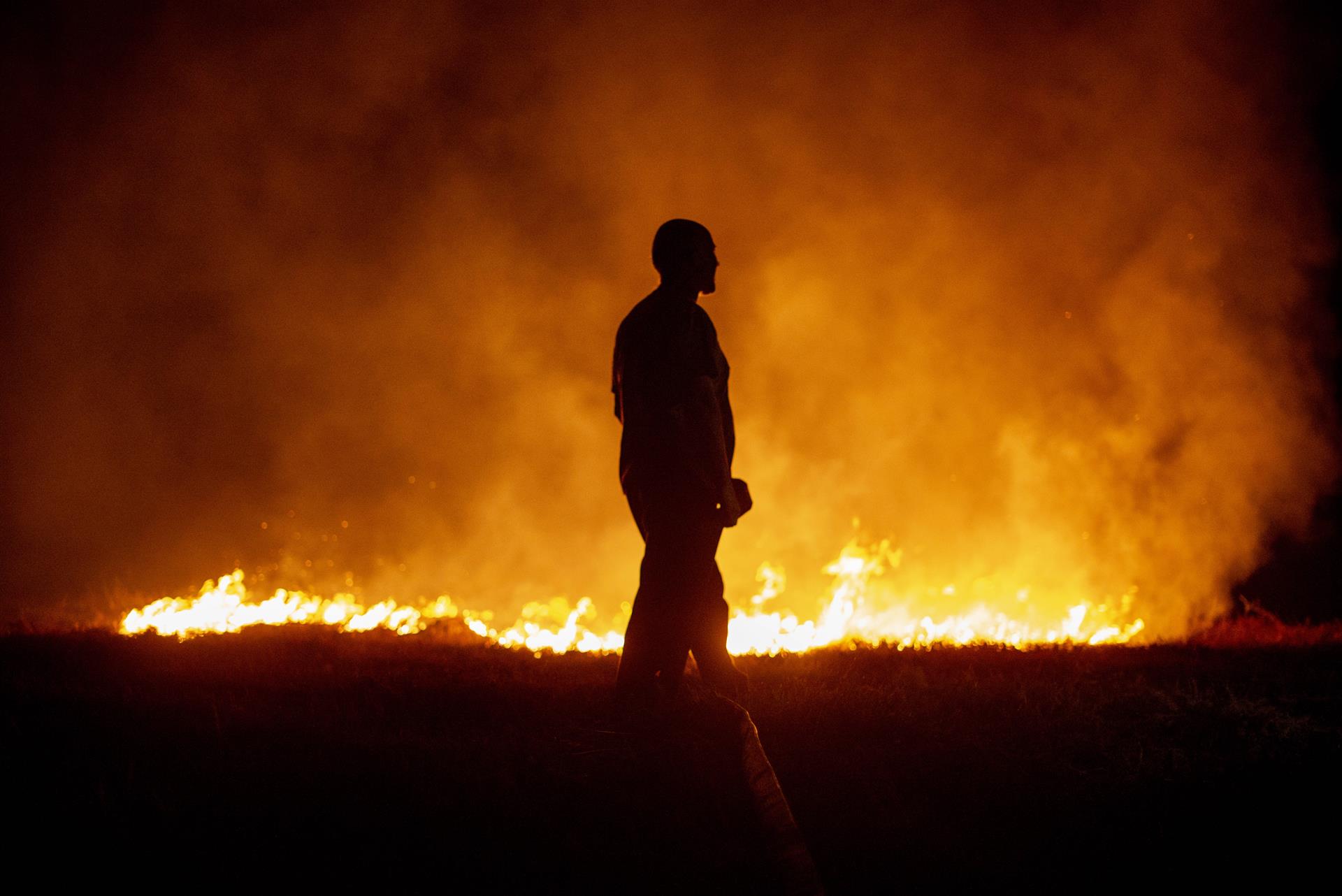 Un vecino ante las llamas mientras colabora en las labores de extinción del incendio de Cures, en Boiro, A Coruña, en la madrugada de este sábado. EFE/Brais Lorenzo