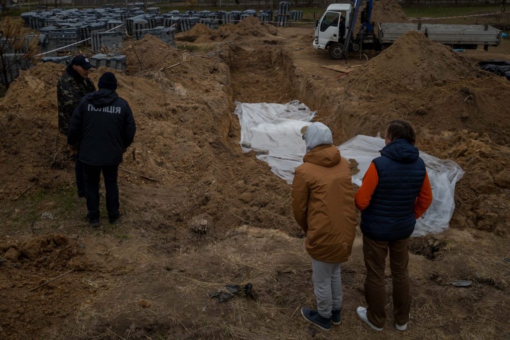 Several people speak with two Ukrainian officers in front of a mass grave in Bucha, Ukraine