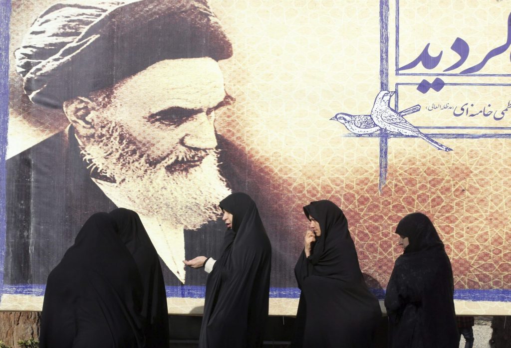 Iraanse vrouwen lopen langs een reclamebord met een foto van ayatollah Ruhollah Khomeini.