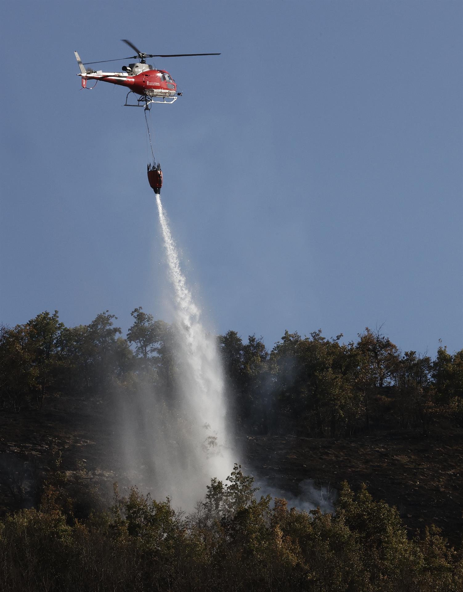 Varias dotaciones de bomberos, con unos treinta efectivos en total, siguen trabajando en el monte Ezkaba, apoyados por un helicóptero, para refrescar puntos calientes del incendio. EFE/Jesus Diges