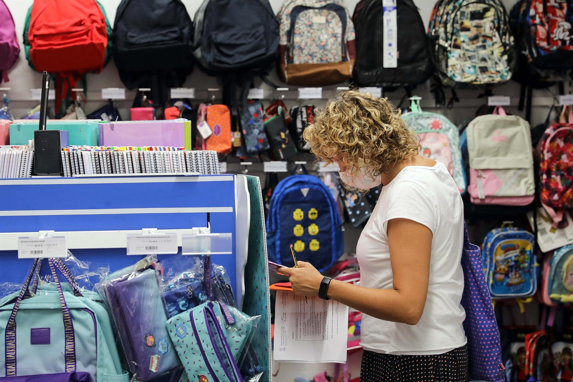 Una mujer, preparada con una lista de material escolar, consulta el precio, en una papelería, de una mochila infantil. EFE