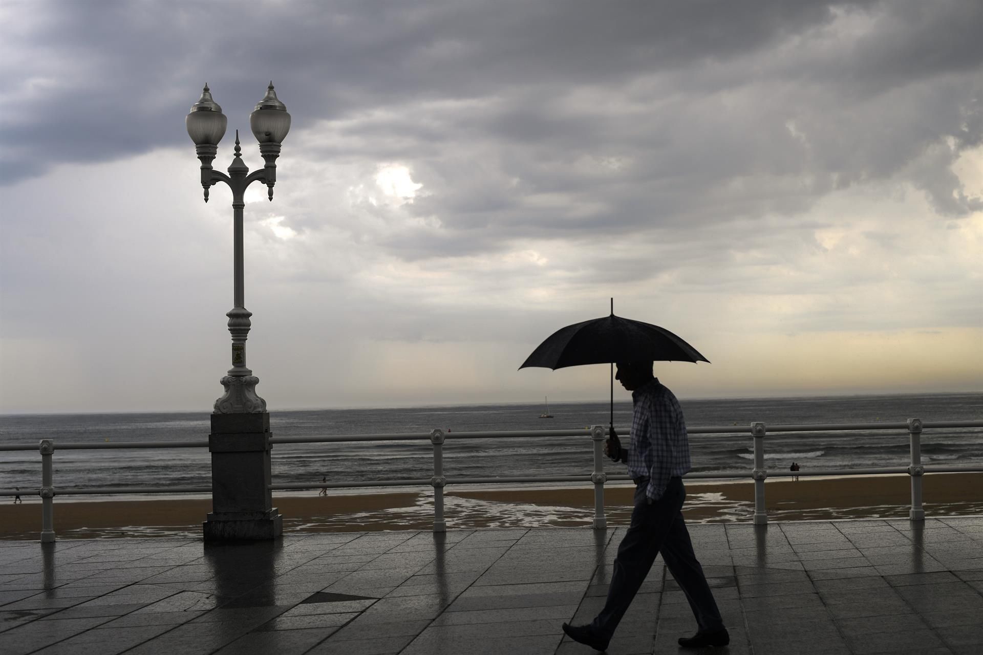 Un hombre se protege con el paraguas de la lluvia, en el paseo de muro de la playa de San Lorenzo de Gijón, en una fotografía de archivo. EFE/ Eloy Alonso