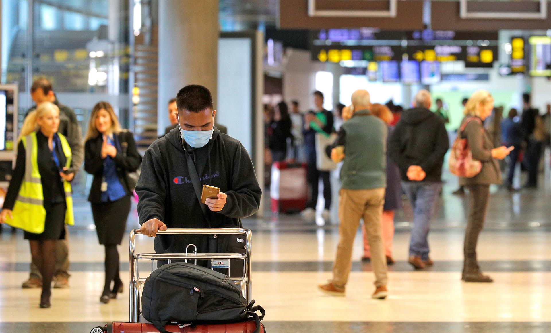 Un viajero recién llegado al aeropuerto de Manises consulta su teléfono móvil protegido con una mascarilla. EFE/Manuel Bruque/Archivo