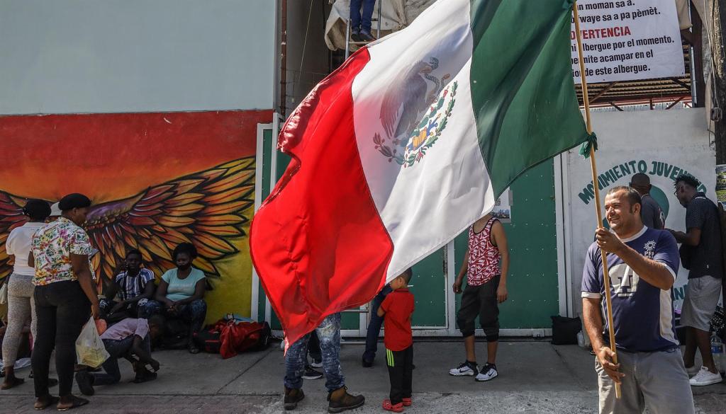 Una persona ondea la bandera de México junto a migrantes de origen haitiano que permanecen afuera del albergue Movimiento Juventud 2000, a la espera de un lugar de hospedaje, el 26 de septiembre de 2022 en la fronteriza Tijuana, Baja California (México). EFE/Joebeth Terriquez
