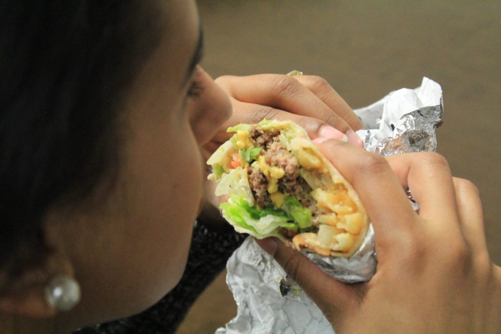 Una mujer come una combinación de burrito mexicano y hamburguesa con patatas fritas. 