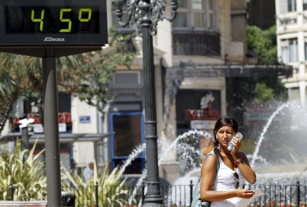 Una joven trata de refrescarse junto a una fuente y un termómetro que marca 45 grados en Madrid