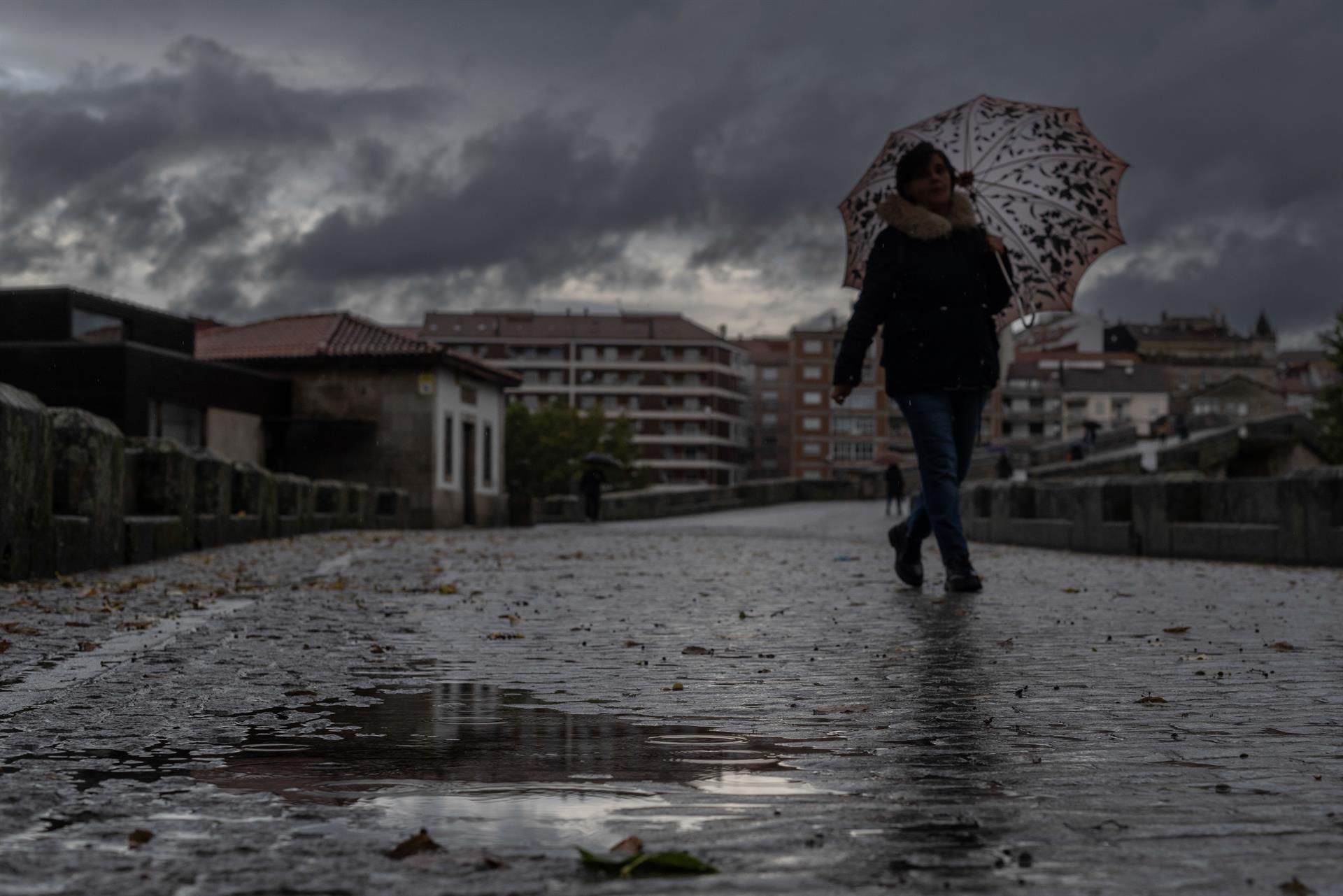 Una mujer se refugia de la lluvia con un paraguas mientras camina por el puente romano de Ourense coincidiendo con la entrada de la borrasca Armand, que ha dejado en Galicia este jueves 190 incidencias. EFE/ Brais Lorenzo