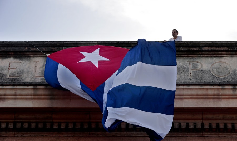 Um jovem coloca uma bandeira de Cuba em im prédio da Universidade de Havana, nesta quinta-feira. EFE/Ernesto Mastrascusa