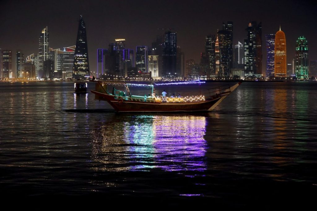 Imagen nocturna de un barco en el agua con el skyline de Qatar de fondo