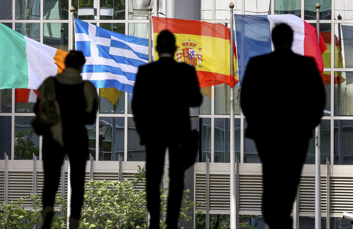 Tres personas se dirigen hacia el Parlamento Europeo en Bruselas, frente a las banderas de (i-d) Irlanda, Grecia, España y Francia.