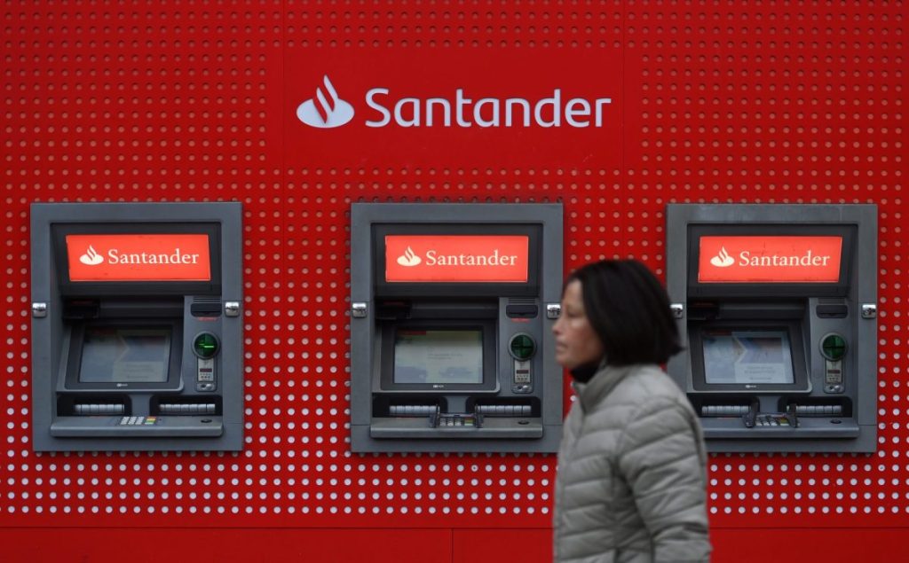 Una mujer pasa junto a cajeros del Banco Santander en Londres