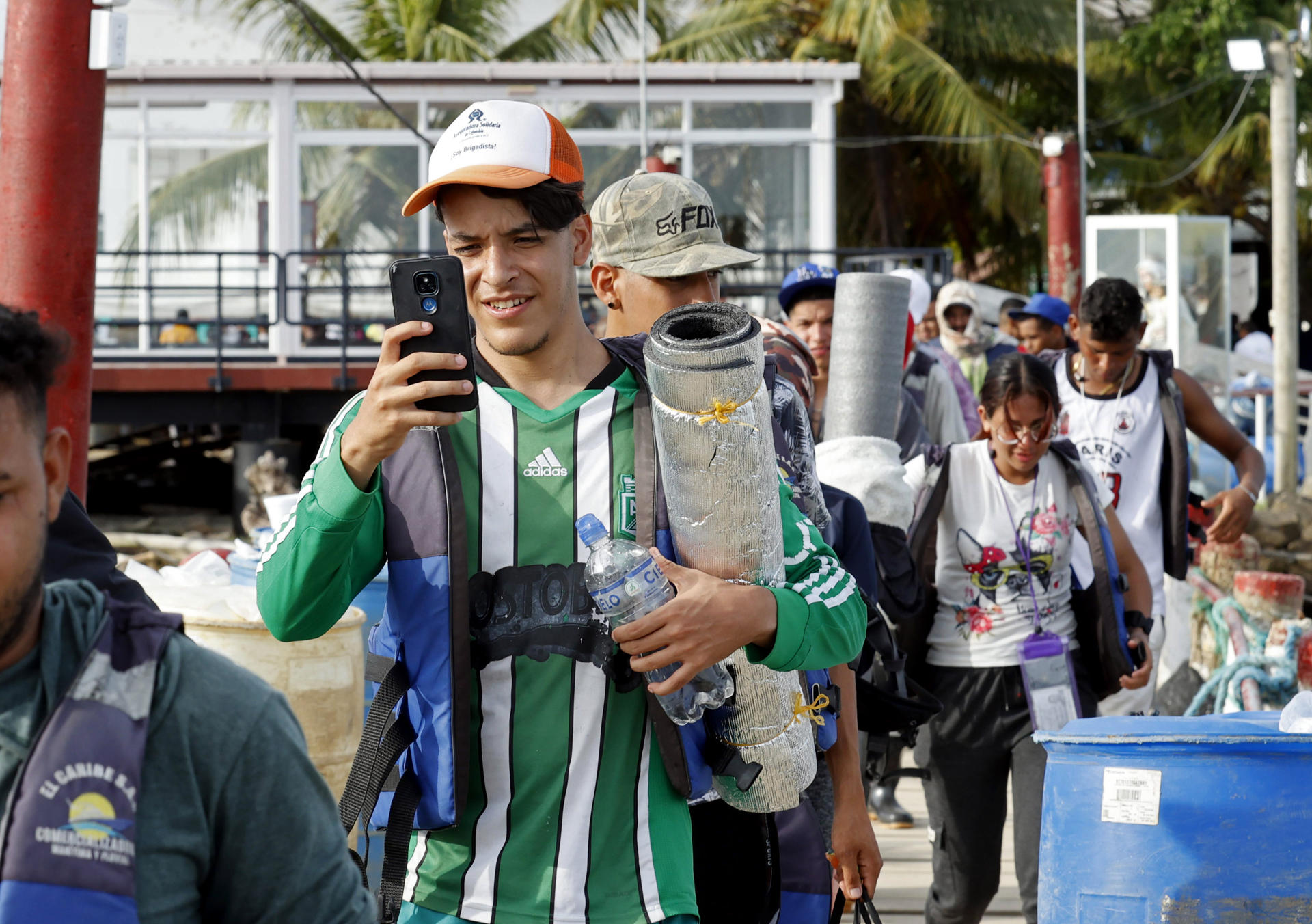 Migrantes usan sus celulares antes de abordar una lancha el 8 de octubre de 2022 en Necoclí (Colombia). EFE/Mauricio Dueñas Castañeda
