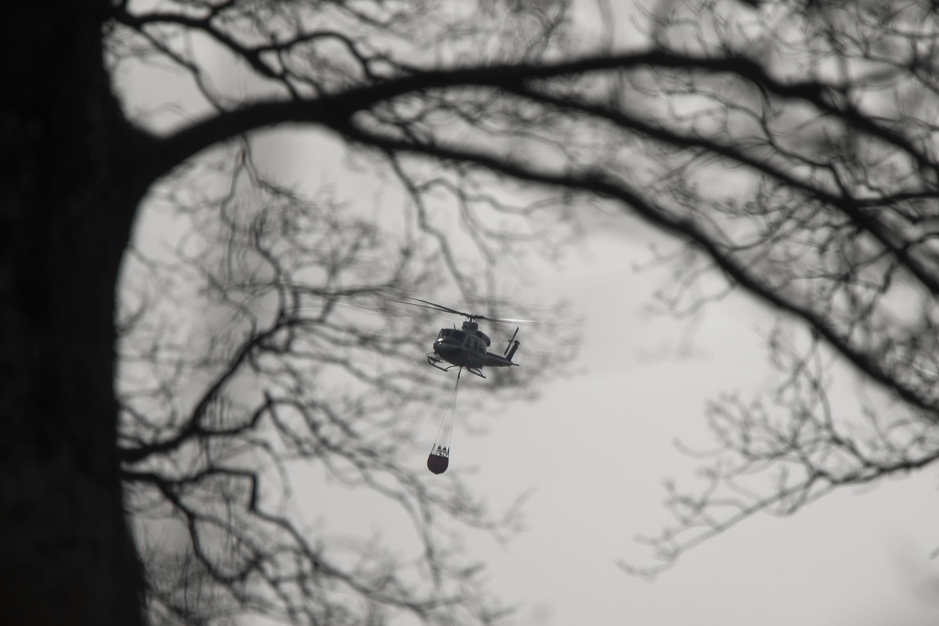 Un helicóptero transporta agua durante los trabajos de extinción de un incendio forestal declarado por una excavadora que trabajaba en los montes próximos a la localidad cántabra de Los Corrales de Buelna, este martes. FOTO/EFE/Pedro Puente Hoyos