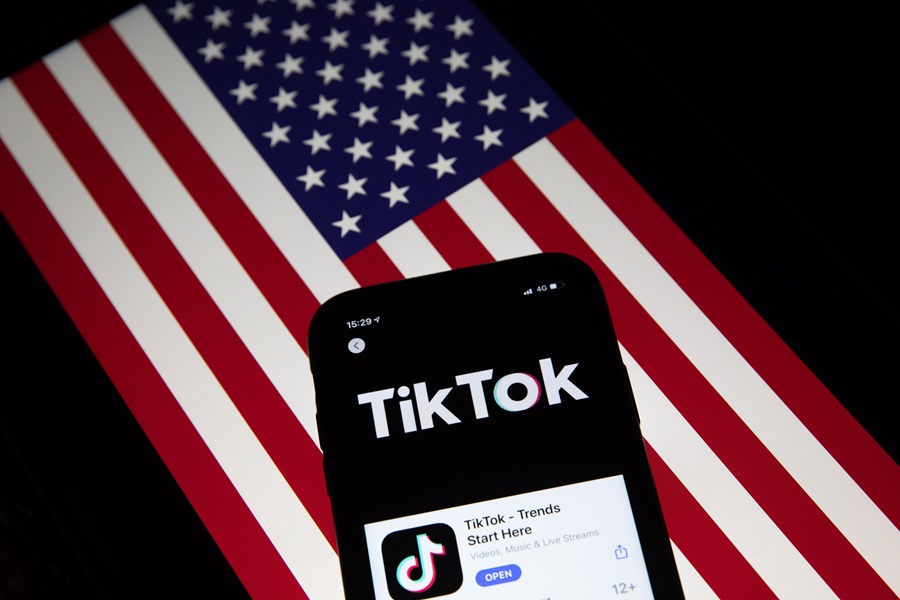 Fotografía de archivo que muestra la aplicación TikTok en la pantalla de un teléfono con la bandera estadounidense de fondo. 