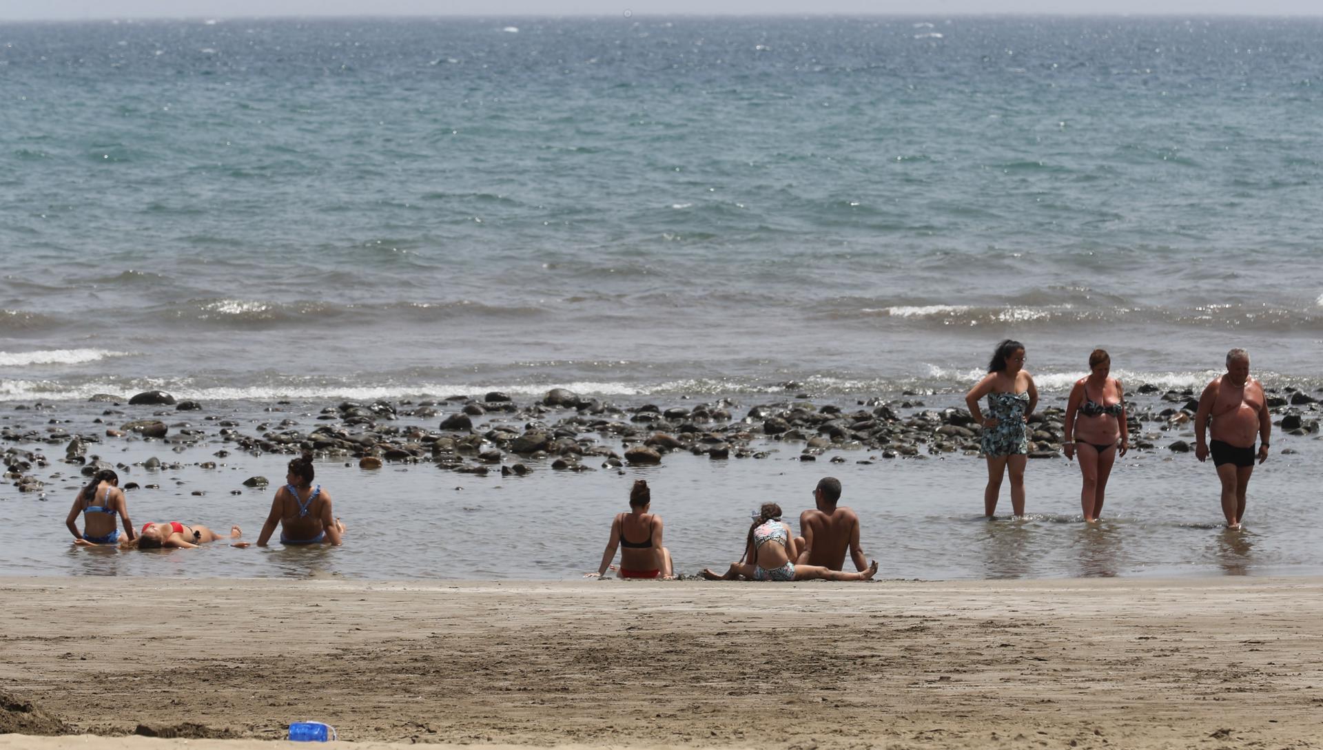 Varias personas se refrescan en una charca formada en la orilla de la playa de Maspalomas, en Gran Canaria. EFE/ Elvira Urquijo A.