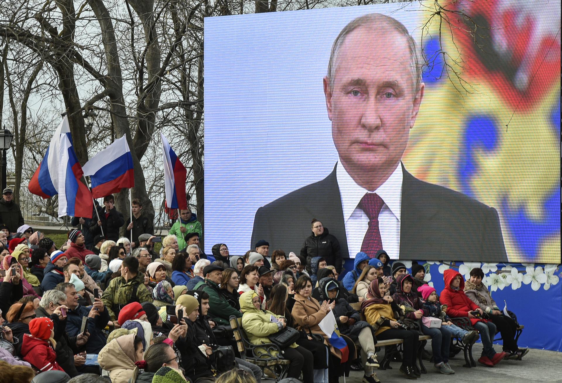 People sit under a screen with Russian President Vladimir Putin as they attend an event on the ninth anniversary of Russia's annexation of Crimea in Sevastopol, Crimea, 18 March 2023. EFE-EPA/STRINGER