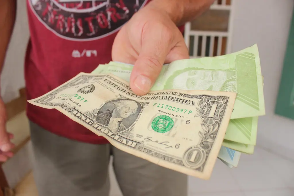 Fotografía de archivo en la que se registró la mano de un hombre que sostiene un billete de un dólar sobre un fajo de bolívares de distintas denominaciones, en San Cristóbal (Táchira, Venezuela). EFE/Johnny Parra