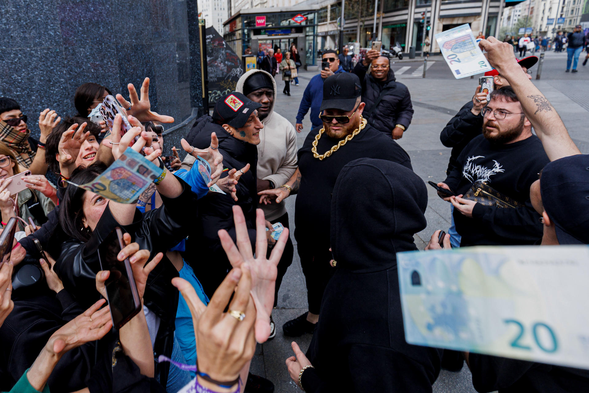 El rapero Yung Beef (c), rodeado de guardaespaldas, lanza billetes reales para promocionar su último trabajo, este jueves en el centro de Madrid. EFE/ Sergio Pérez