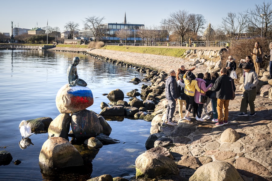 Un grupo de personas se hace una foto con la  Sirenita de Copenhague, que amaneció hoy con la bandera de Rusia pintada en su base. 
