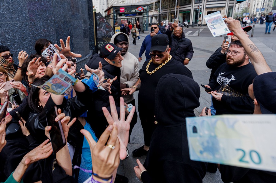 El rapero Yung Beef (c), rodeado de guardaespaldas, lanza billetes reales para promocionar su último trabajo, este jueves en el centro de Madrid.