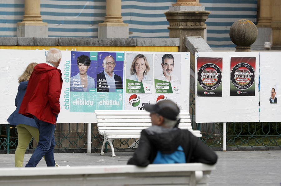 Unos ciudadanos observan varios carteles electorales este martes en San Sebastián tras conocerse el comunicado de los siete condenados por asesinatos de ETA.