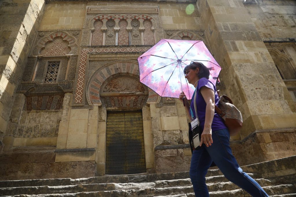 Una mujer se resguarda del sol con una sombrilla mientras camina junto a la Mezquita-Catedral de Córdoba