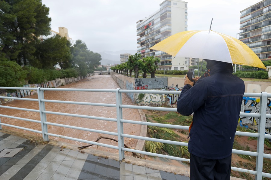 Una persona toma imágenes del caudal en un barranco cuando el episodio de lluvias torrenciales ha dejado un registro histórico en en Benicàssim.
