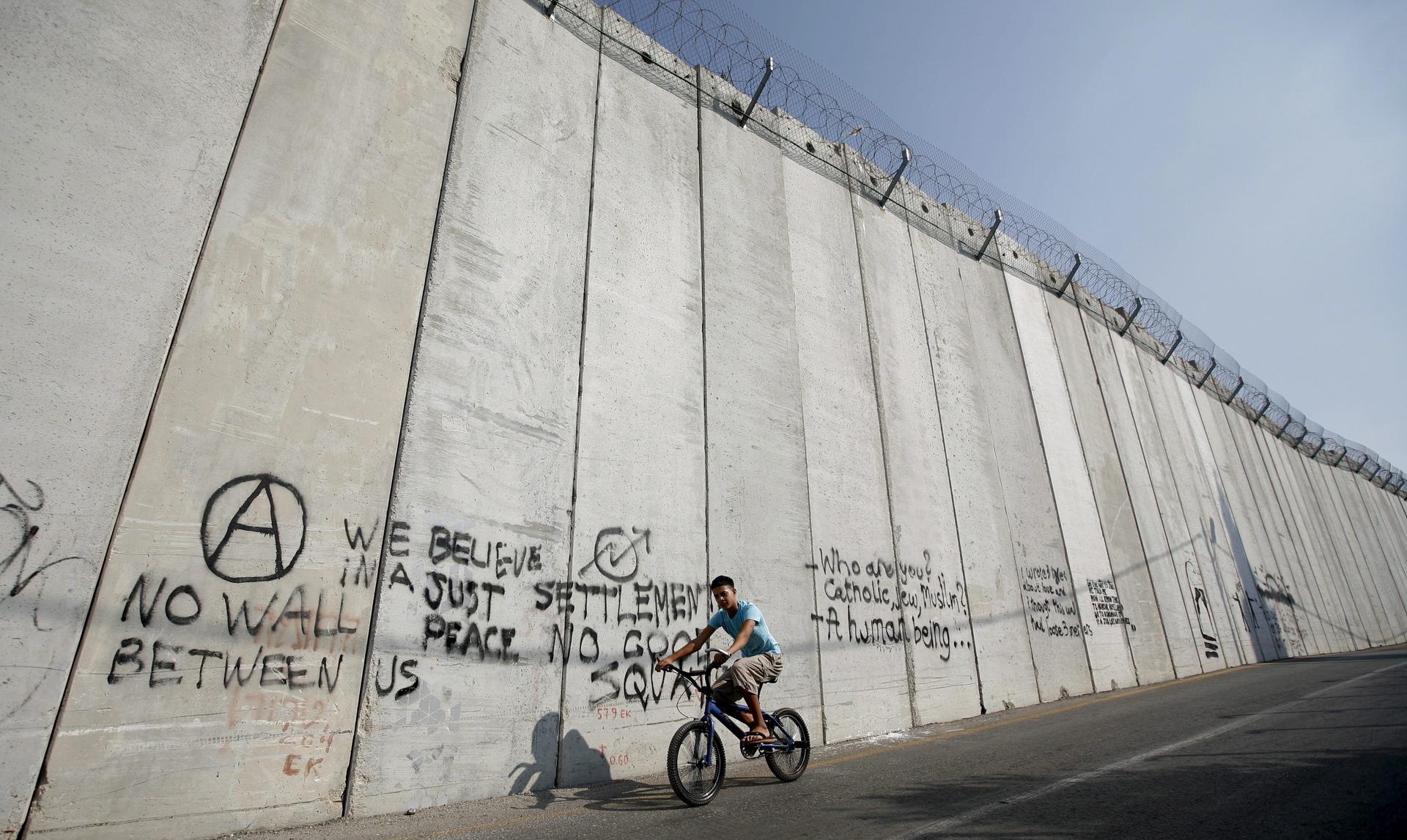 An Arab boy rides his bike next to the separation wall between the Israel and Palestine in east Jerusalem, on 23 August 2010. EPA/OLIVER WEIKEN/FILE