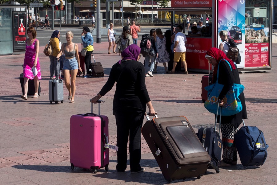 Varios turistas se llevan sus maletas por la Plaza España de Barcelona. El turismo en la campaña del 28M