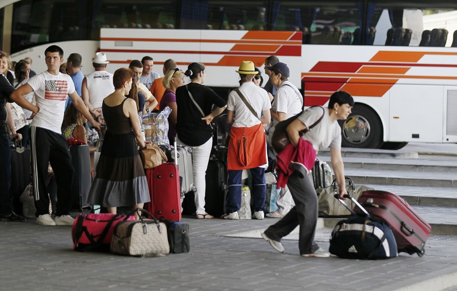 Varios viajeros esperan con sus maletas a la llegada de sus autocares.