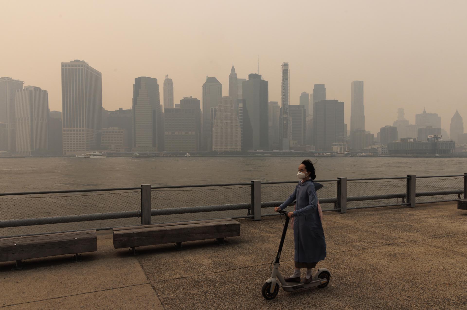 A person wearing a mask and riding scooter passes as buildings in lower Manhattan are seen through smoke filling the air from wildfires burning in Canada, in the Brooklyn borough of New York, New York, USA, 07 June 2023. EFE/EPA/JUSTIN LANE
