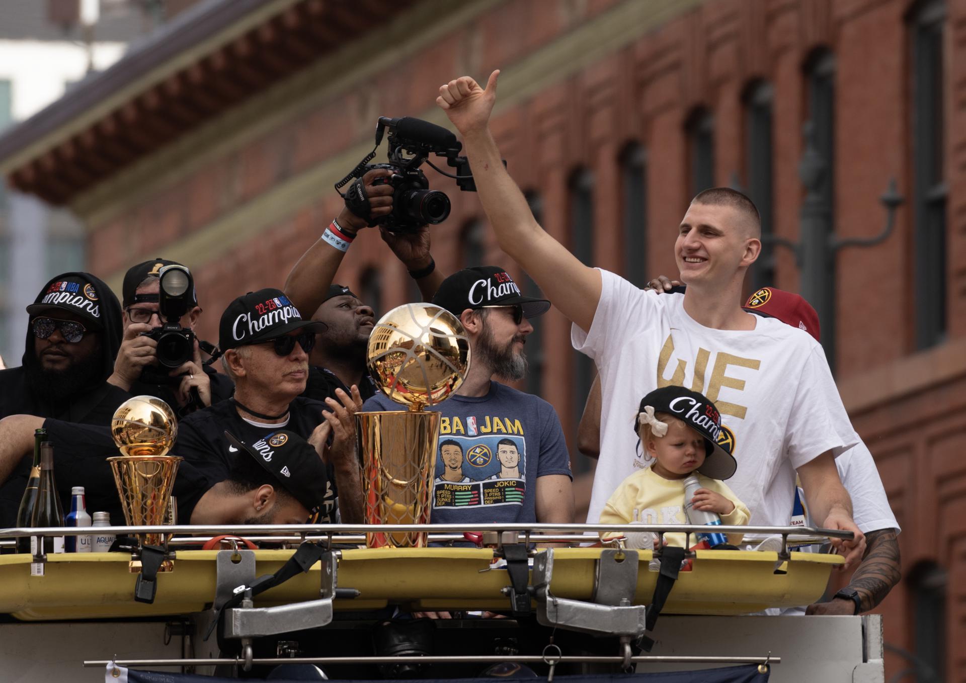 El pívot de los Denver Nuggets Nikola Jokic (d) encabeza el acto de celebración del título de la NBA, este 15 de junio de 2023, a bordo de un camión de bomberos junto al trofeo de campeones y el de MVP, en Denver Colorado (EE.UU.). EFE/Bob Pearson