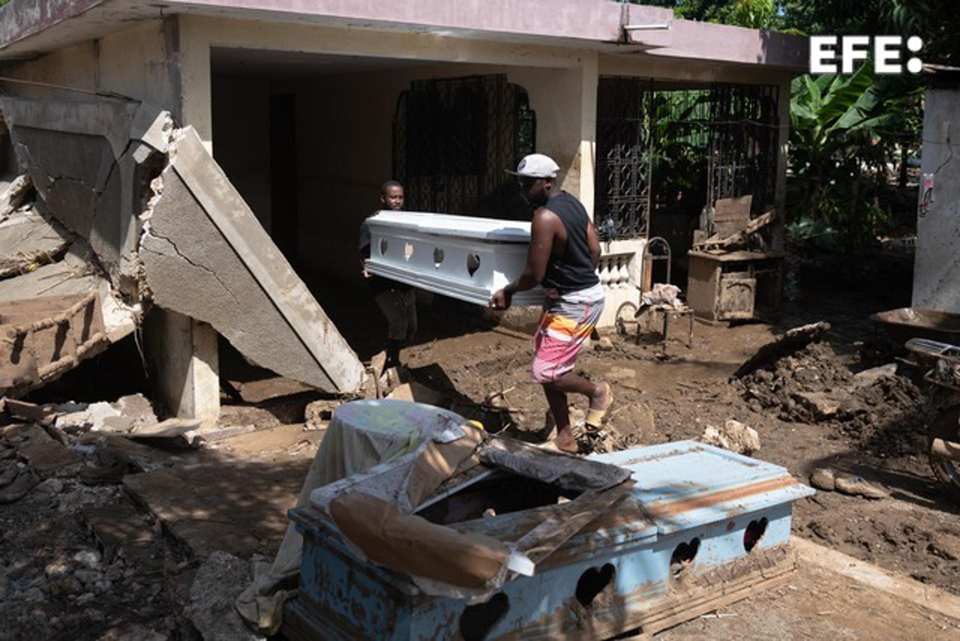 Two men carry a crate next to a damaged house on a muddy street from heavy rains, in Leogane, Haiti, 06 June 2023. EFE/ Johnson Sabin

