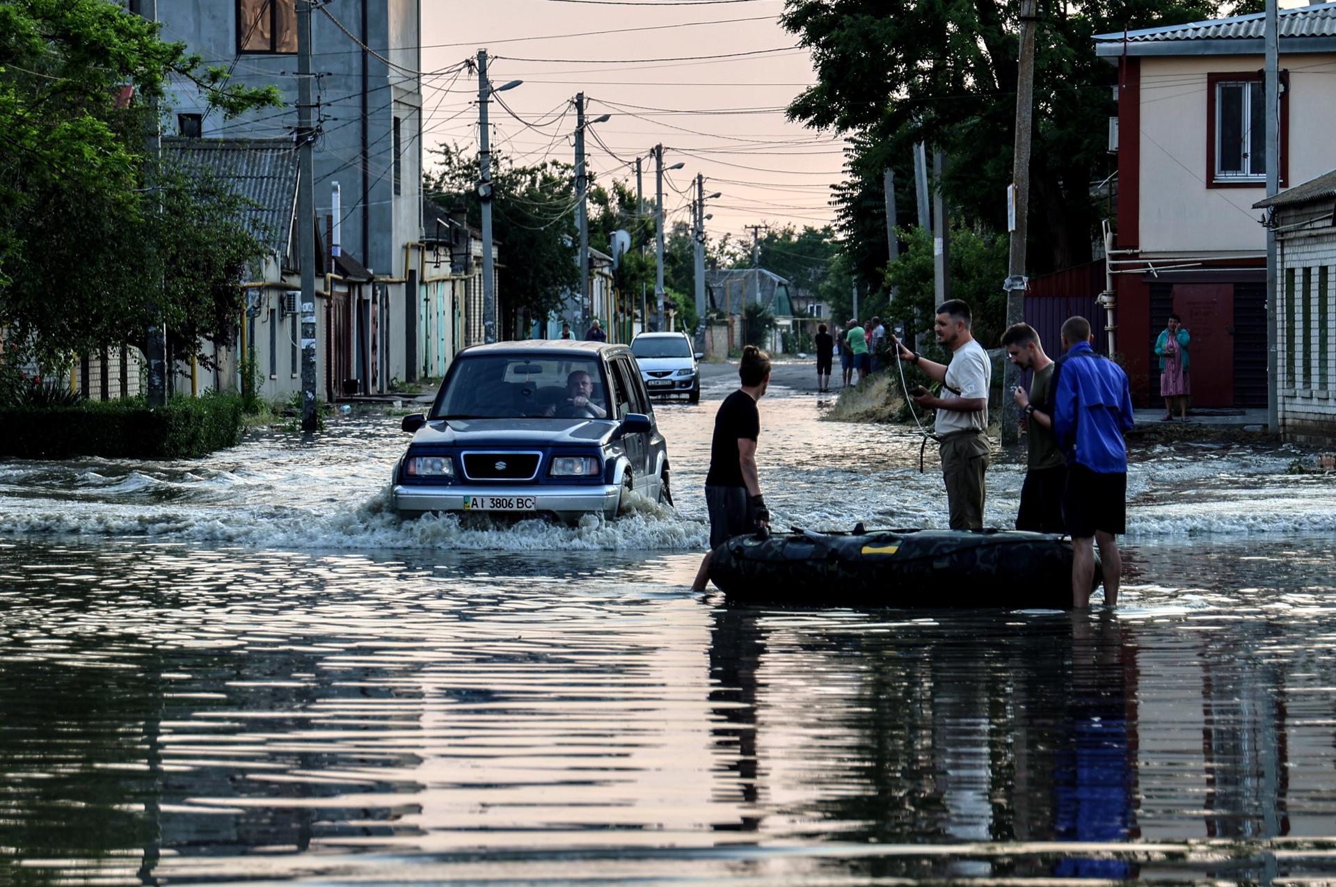 People stand next to an inflatable boat as a car drives past them in a flooded street of Kherson, Ukraine, 06 June 2023. EFE-EPA/IVAN ANTYPENKO
