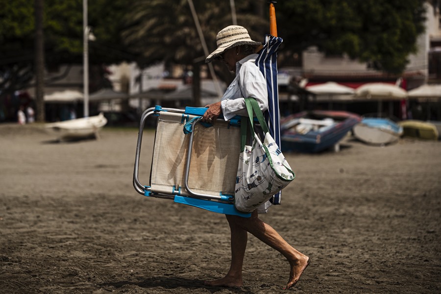 A woman carrying a chair and umbrella goes to El Palo beach in Malaga.