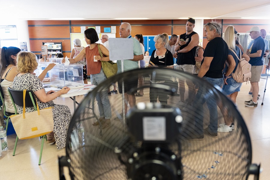 Varios votantes hacen cola ante su mesa electoral situada cerca de un ventilador para combatir el calor en un colegio electoral de la localidad de Pineda de Mar.