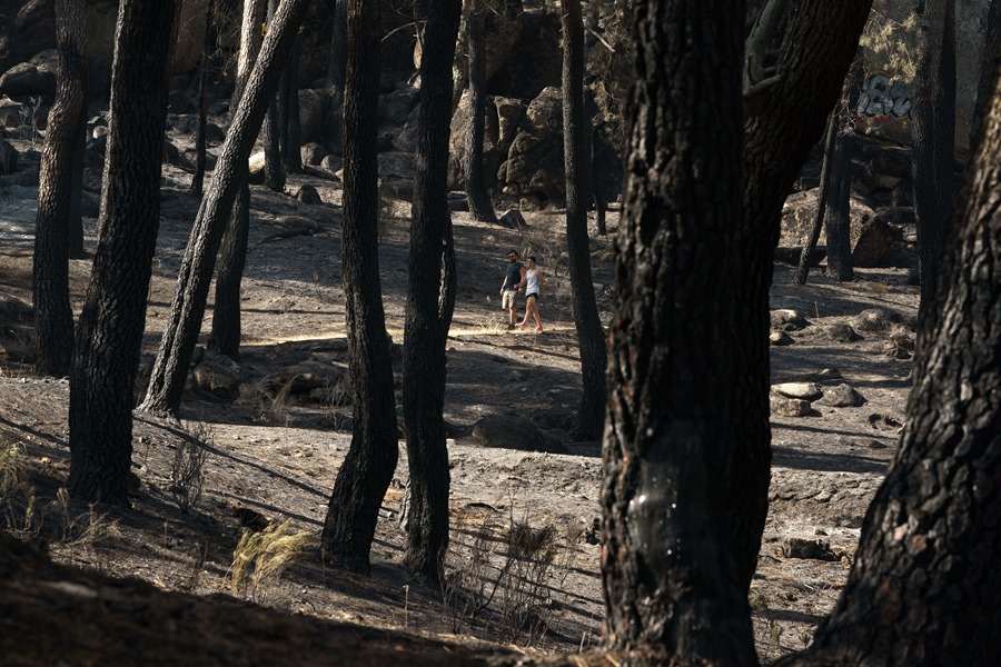 Dos personas pasan por el área recreativa de "El Batán" de la localidad abulense de El Hoyo de Pinares, afectada por un incendio