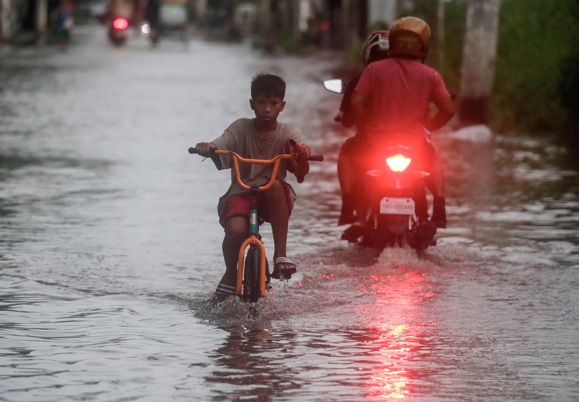 A Filipino boy rides a bicycle amidst a street partially submerged by the floodwater in Malabon city, Metro Manila, Philippines, 26 July 2023. EFE-EPA/FRANCIS R. MALASIG
