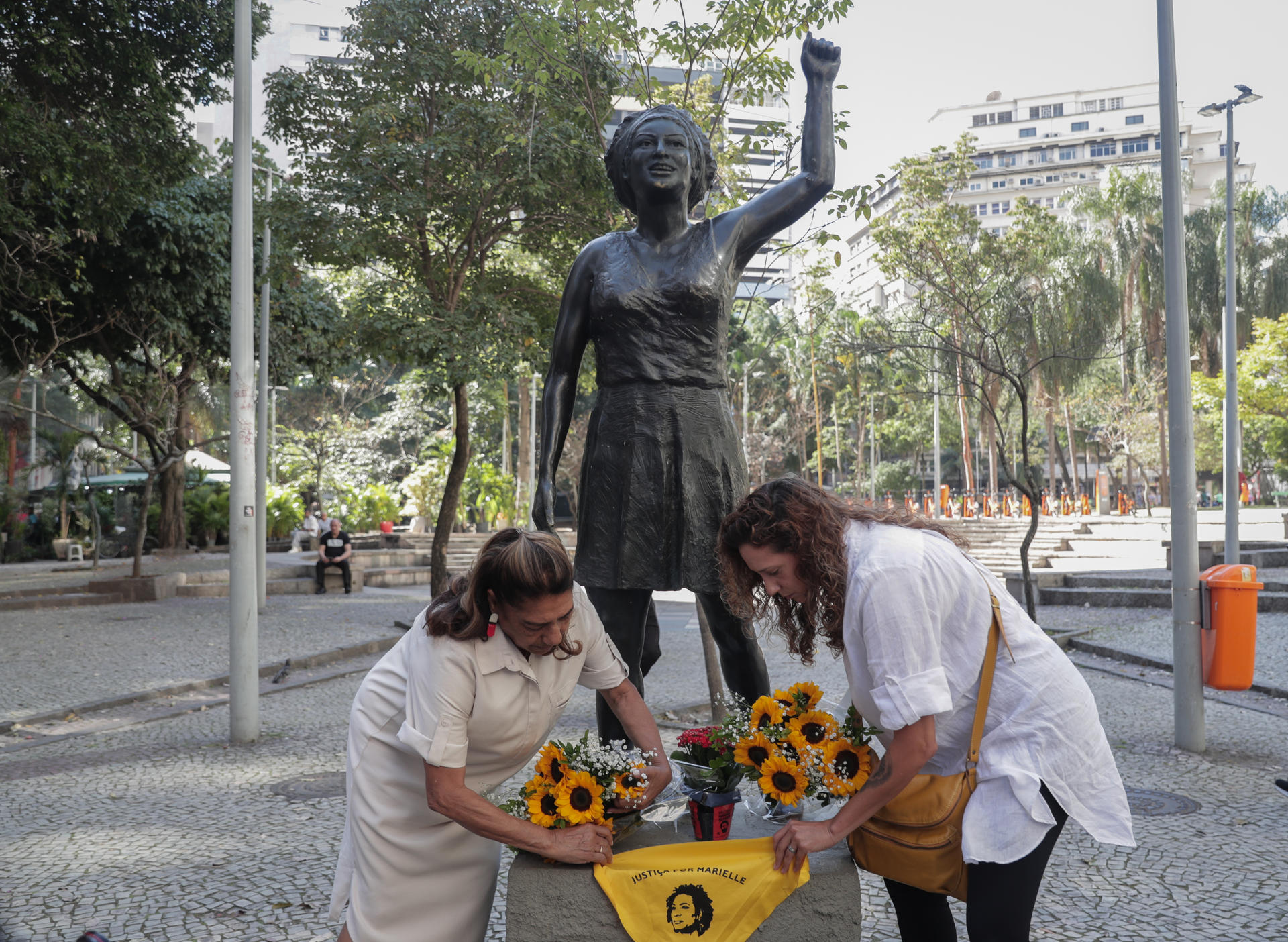 Mônica Benício (d) y Marinete da Silva (i), viuda y madre, respectivamente, de la concejala asesinada Marielle Franco, colocan flores y un pañuelo en su estatua durante un homenaje por el día de su cumpleaños, hoy, en Río de Janeiro (Brasil). EFE/André Coelho