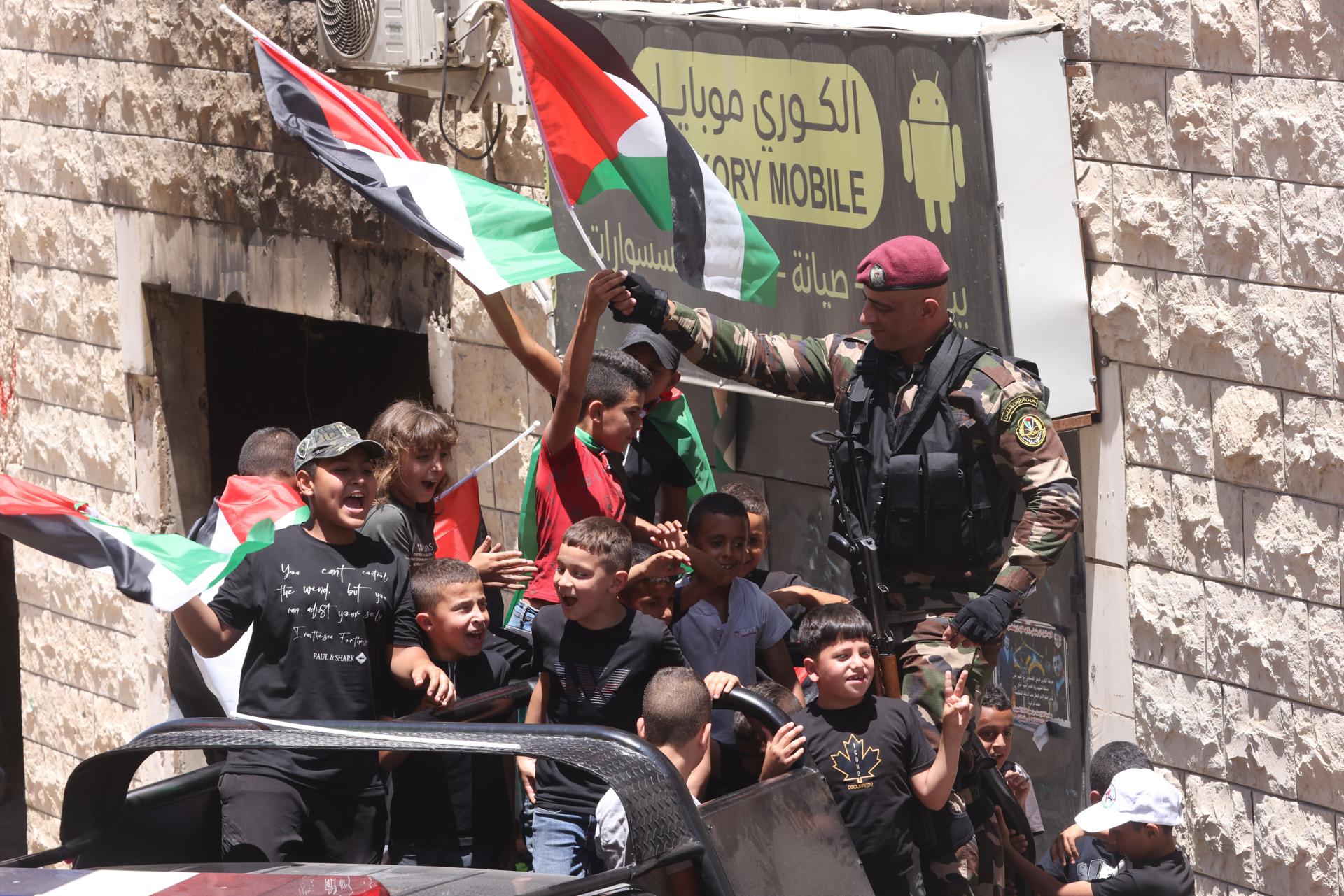 Seguranças paletinos e crianças com bandeiras cumprimentam o presidente Mahmoud Abbas durante sua visita a Jenin nesta quarta-feira. EFE/ALAA BADARNEH