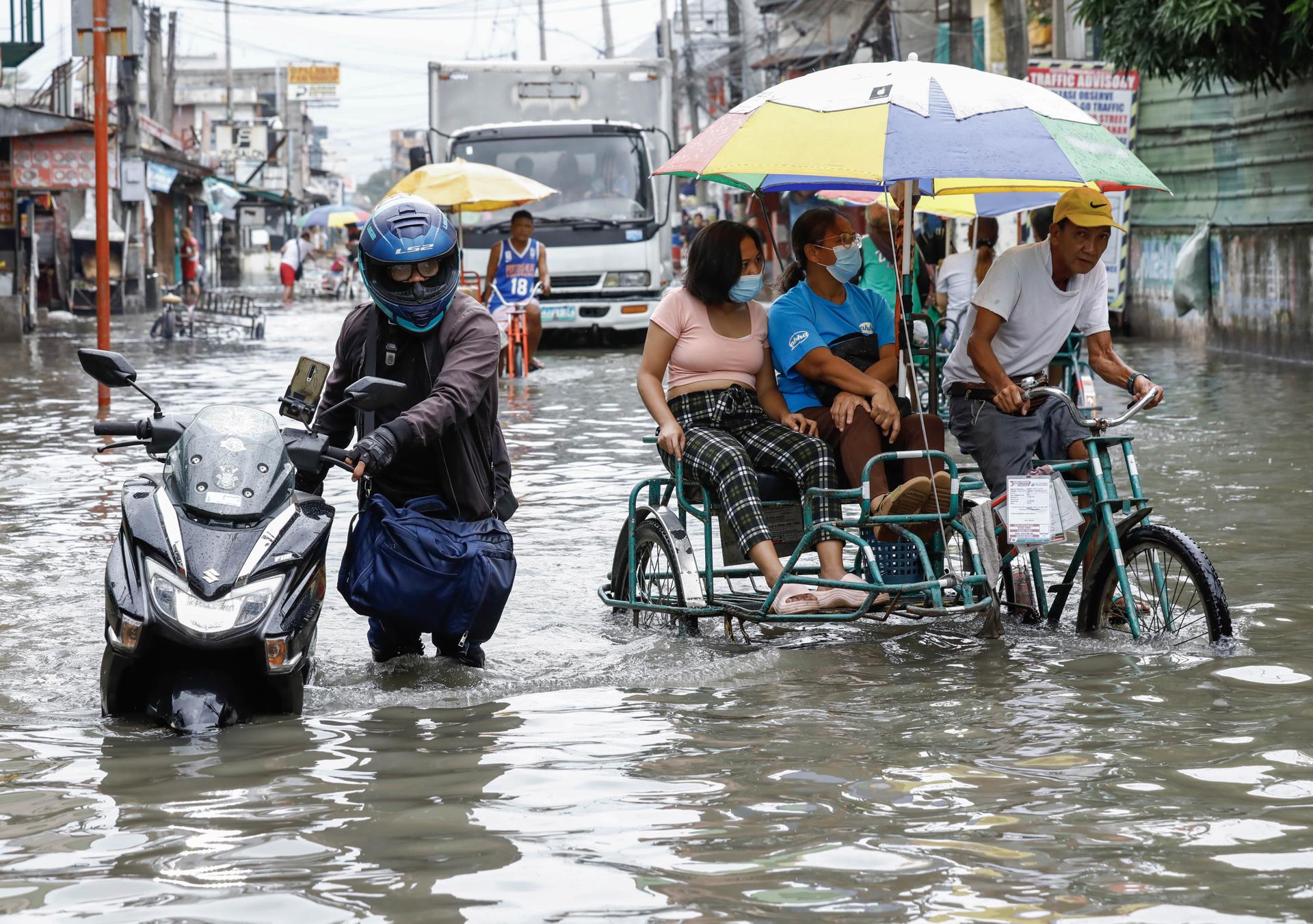A man (L) pushes his motorcycle through a flooded road as other residents ride a tricycle in Valenzuela City, Metro Manila, Philippines, 27 July 2023. EFE-EPA/ROLEX DELA PENA
