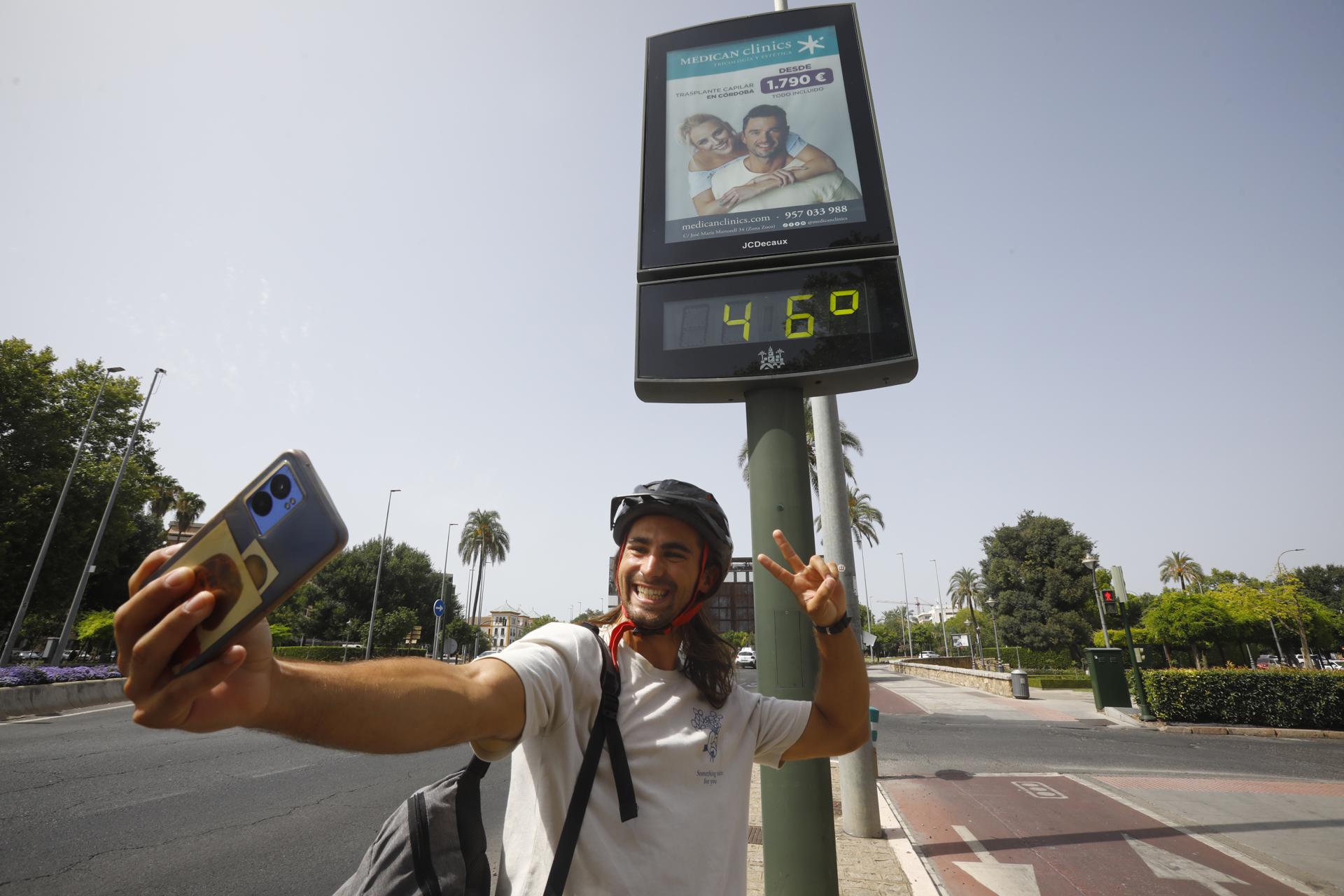 Un joven se fotografía delante de un termómetro de calle en Córdoba que marca 46 grados. EFE/Salas