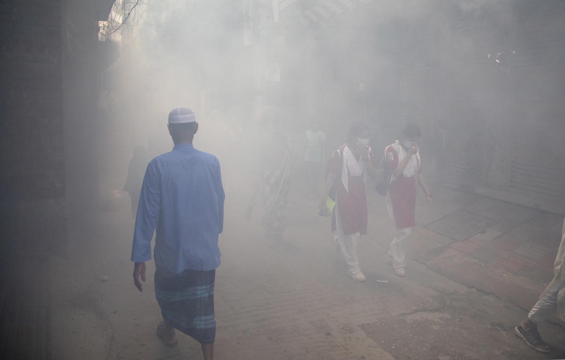 People walk along on the smoky road as the Dhaka South City Corporation (DSCC) worker sprays insecticides to kill mosquitos in Dhaka, Bangladesh, 10 July 2023. EFE-EPA FILE/MONIRUL ALAM