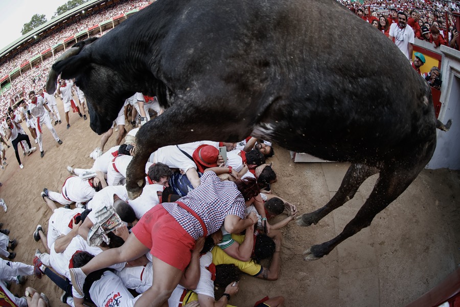 Una vaquilla salta por encima de un grupo de corredores en la plaza de toros tras el tercer encierro de los Sanfermines 2023, este domingo en Pamplona.