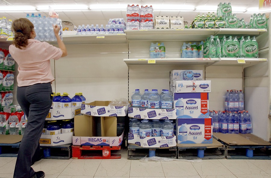 Una trabajadora repone botellas de agua en los estantes de un supermercado.
