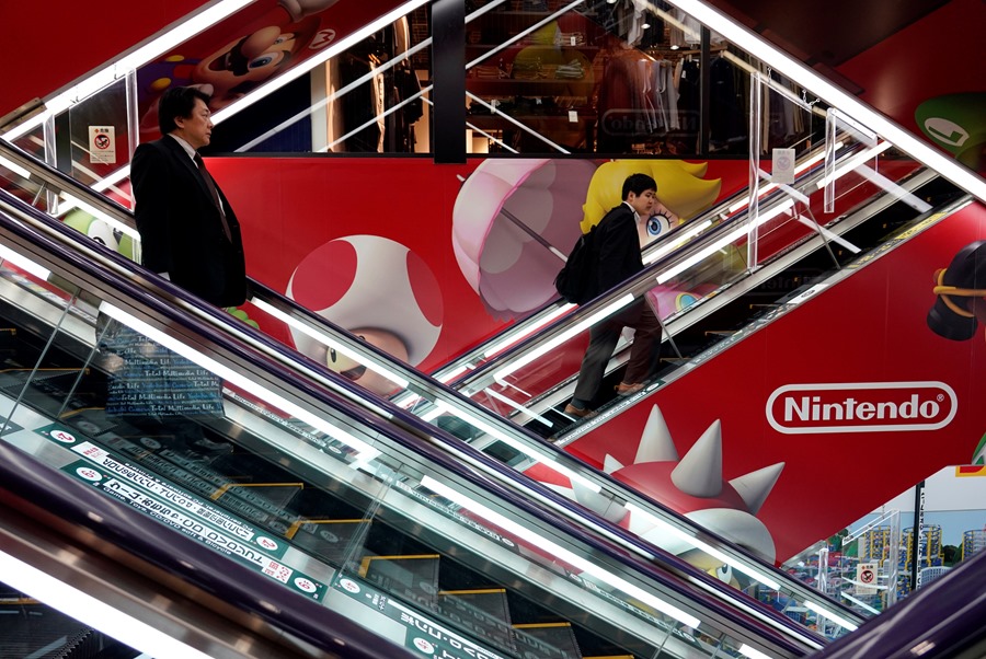 Dos hombres caminan por escaleras mecánicas frente a un anuncio de la empresa Nintendo, en Japón.