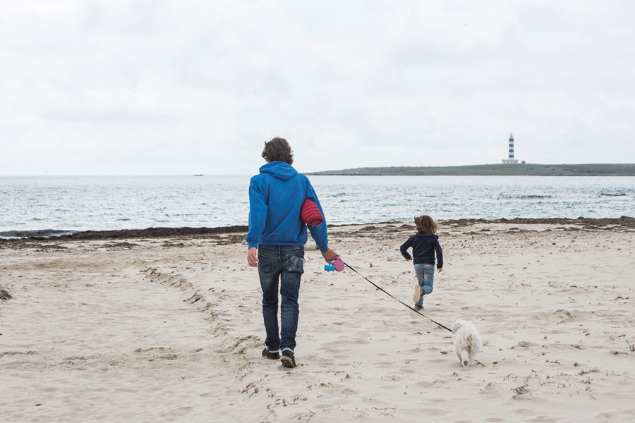 Una padre, su hija y su perro pasean por la playa Punta Prima de Menorca. 