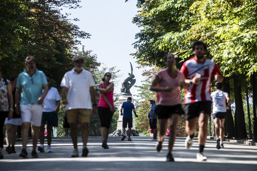 Varias personas pasean junto al Ángel Caido en el parque de El Retiro en Madrid.
