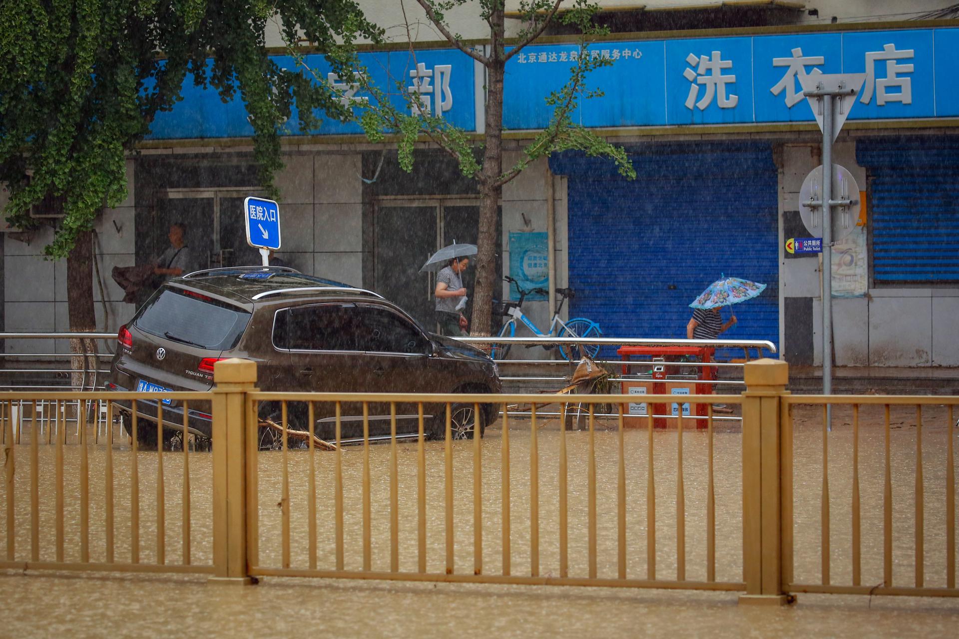 People walk next to a car damaged by floods during a downpour in Mentougou District, west of Beijing, China, 01 August 2023. EFE-EPA/MARK R. CRISTINO