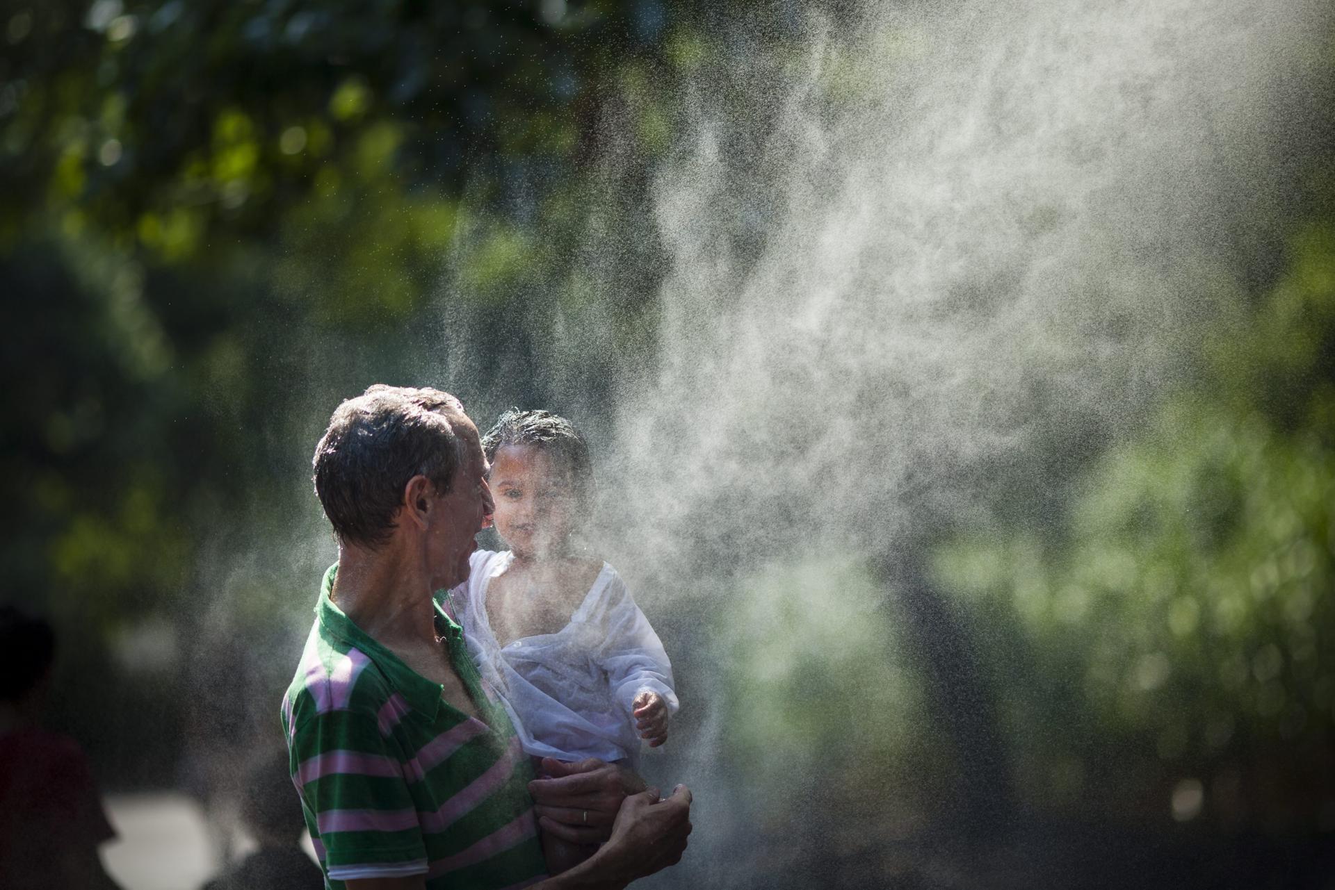 Un hombre y su hija refrescan con agua ante las altas temperaturas que se registran en una ola de calor, en una fotografía de archivo. EFE/Jim Lo Scalzo